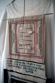 Den relasjonsdreptes likskjorte av Karin Osbakk: hvit likskjorte med brodert felt, sølvskjeer og tekstbord